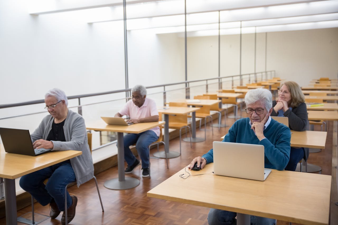 Elderly people enthusiastically using laptops in a classroom environment, embracing modern technology.